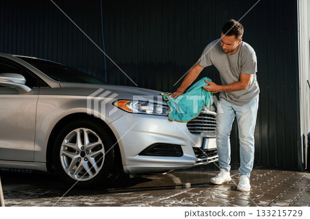 View from the side, using cloth to polish the automobile. Man is with his car outdoors View from the side, using cloth to polish the automobile. Man is with his car outdoors 133215729