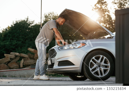 Hood is opened, repairing. Man is with his car outdoors 133215834