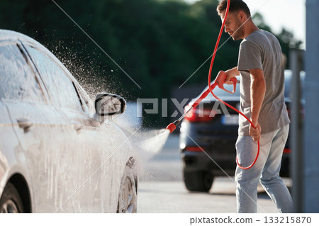 Water high pressure stream, car wash. Man is with his automobile outdoors Water high pressure stream, car wash. Man is with his automobile outdoors 133215870