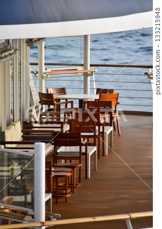 Outdoor seats on passenger ship deck with the calm seascape. Cruise ship deck. Wooden promenade deck on a luxury cruise liner. Ocean in background. 133215948