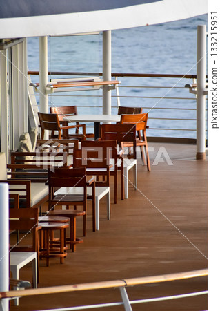 Outdoor seats on passenger ship deck with the calm seascape. Cruise ship deck. Wooden promenade deck on a luxury cruise liner. Ocean in background. 133215951