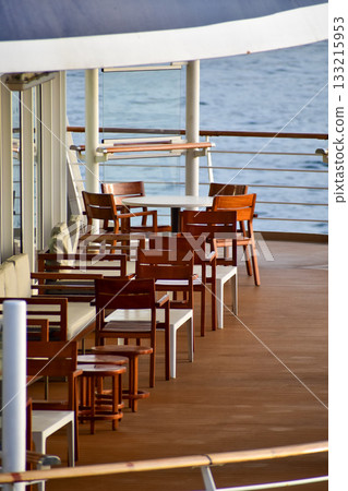 Outdoor seats on passenger ship deck with the calm seascape. Cruise ship deck. Wooden promenade deck on a luxury cruise liner. Ocean in background. 133215953