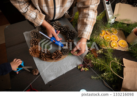 Family Crafting Christmas Wreath With Pinecones, Citrus And Greenery At Home Family Crafting Christmas Wreath With Pinecones, Citrus And Greenery At Home 133216098