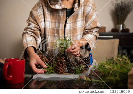 Cozy Home Christmas Craft: Person Arranging Pine Cones and Greenery for Decor Cozy Home Christmas Craft: Person Arranging Pine Cones and Greenery for Decor 133216099