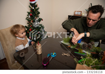 Family Christmas Craft Scene: Dad Decorating Pine Branches While Child Watches 133216118