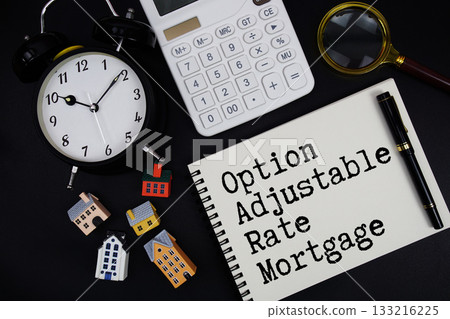 Notepad with the phrase "Option Adjustable Rate Mortgage" surrounded by a pen, calculator, magnifying glass, clock, and house model 133216225