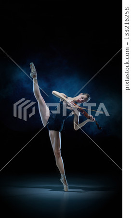 Female ballerina in leg extension while playing violin on dark theatre stage Female ballerina in leg extension while playing violin on dark theatre stage 133216258