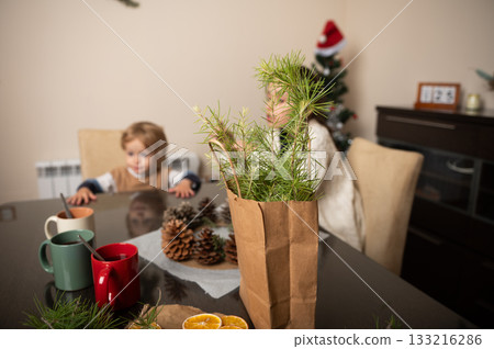 Festive Table Scene With Paper Bag Pine Branches For Christmas Decor And Family Festive Table Scene With Paper Bag Pine Branches For Christmas Decor And Family 133216286