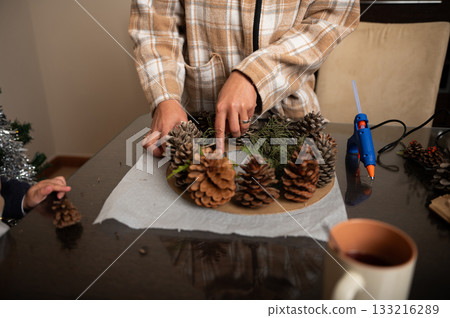 Family Decorating Pinecone Wreath With Pine Cones And Greenery At Home 133216289