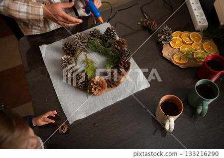 Family Crafting Christmas Wreath With Pinecones and Dried Oranges At Cozy Table Family Crafting Christmas Wreath With Pinecones and Dried Oranges At Cozy Table 133216290