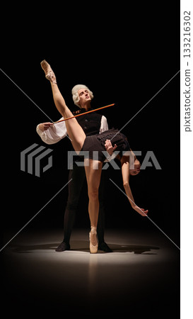 Dancer lifted in sculptural instrument-like extension by classical mentor on dark stage 133216302