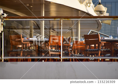 Outdoor seats on passenger ship deck with the calm seascape. Cruise ship deck. Wooden promenade deck on a luxury cruise liner. Ocean in background. 133216309