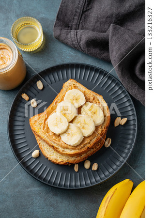 Peanut butter toast and banana on a black plate on a dark background with nuts 133216327