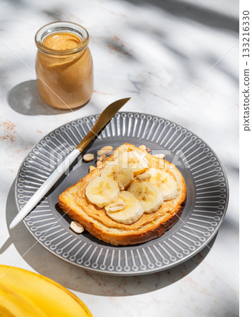 Peanut butter toast and banana on a dark plate on a marble background with fruits Peanut butter toast and banana on a dark plate on a marble background with fruits 133216330