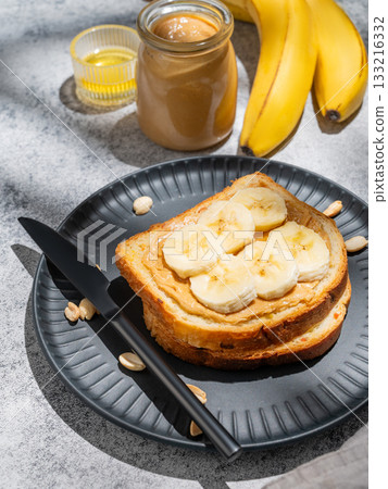 Peanut butter toast and banana on a black plate on a gray background with nuts Peanut butter toast and banana on a black plate on a gray background with nuts 133216332