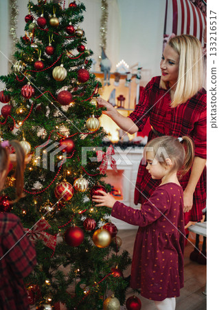 Mother and daughter decorating Christmas tree together at home 133216517