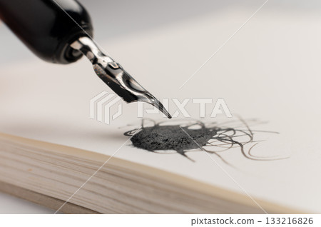 A close-up macro shot of a drop of ink on a notepad. A fountain pen is nearby. Retro office concept. A close-up macro shot of a drop of ink on a notepad. A fountain pen is nearby. Retro office concept. 133216826