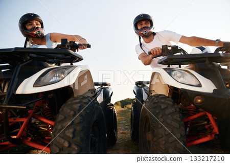 Front view. Man and woman are on ATV outdoors Front view. Man and woman are on ATV outdoors 133217210