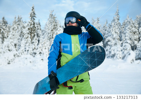 Portrait of man at  ski resort on the background mountains holds snowboard. Wearing ski glasses 133217313