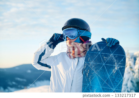 Portrait Of Woman Holding a Snowboard And Wearing Ski Glasses. Ski Goggles Of Snowboarder With The Reflection Of Snowed Mountains. Winter Sports Portrait Of Woman Holding a Snowboard And Wearing Ski Glasses. Ski Goggles Of Snowboarder With The Reflection Of Snowed Mountains. Winter Sports 133217317