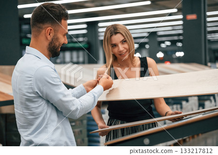 Making fun, color of parquet is the same as girlfriend hair. Man with woman are in the hardware store 133217812