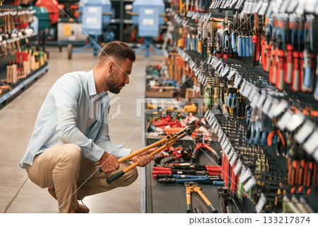Orange colored wire cutter, holding in hands. Man is in the hardware shop Orange colored wire cutter, holding in hands. Man is in the hardware shop 133217874