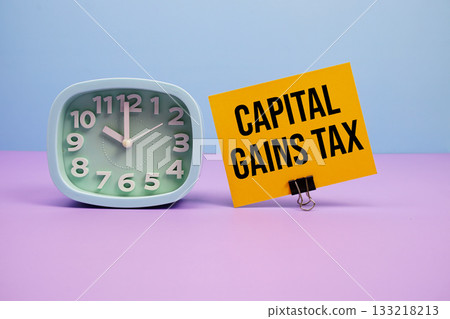 Capital Gains Tax text and alarm clock on blue and purple background Capital Gains Tax text and alarm clock on blue and purple background 133218213