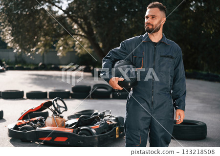 Standing and holding safety helmet. Man is outdoors, kart racing conception 133218508