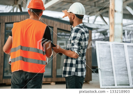 Builder is talking with manager or architect. Two workers are in the industrial wooden warehouse 133218903