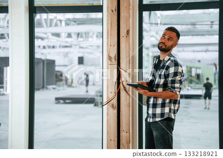 Showing the wooden house that is under construction. Industrial worker in warehouse Showing the wooden house that is under construction. Industrial worker in warehouse 133218921