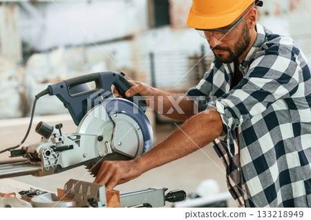 Using the saw to cut the wood. Industrial worker in warehouse Using the saw to cut the wood. Industrial worker in warehouse 133218949