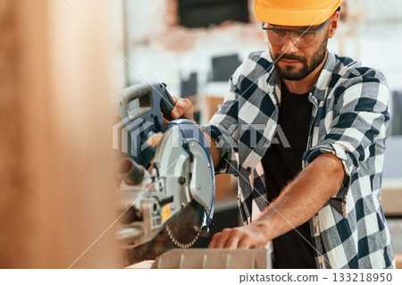 Using the saw to cut the wood. Industrial worker in warehouse 133218950