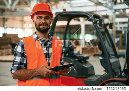 Forklift is behind, digital tablet in hands. Industrial worker in wooden warehouse 133218965