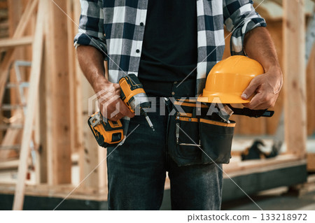 Building the house, holding hard hat and drill. Industrial worker in wooden warehouse Building the house, holding hard hat and drill. Industrial worker in wooden warehouse 133218972