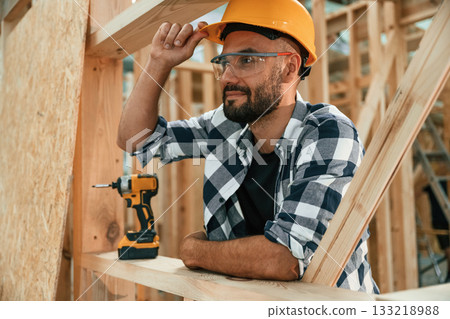 Leaning on the unfinished wooden house, building. Industrial worker in warehouse 133218988