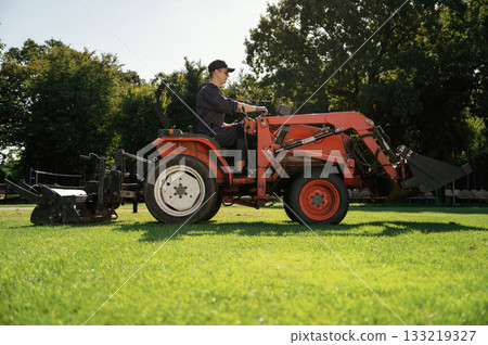 Man is with utility tractor with grass cutter and aerator equipment on the field 133219327