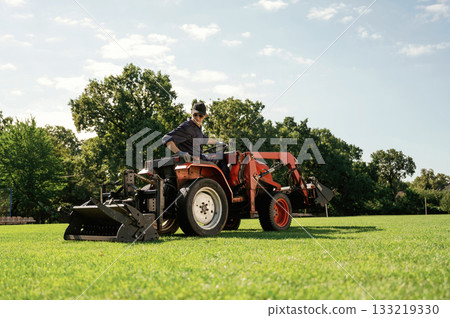 Loan work. Man is with utility tractor with grass cutter and aerator equipment on the field 133219330