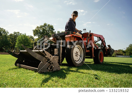Loan work. Man is with utility tractor with grass cutter and aerator equipment on the field Loan work. Man is with utility tractor with grass cutter and aerator equipment on the field 133219332