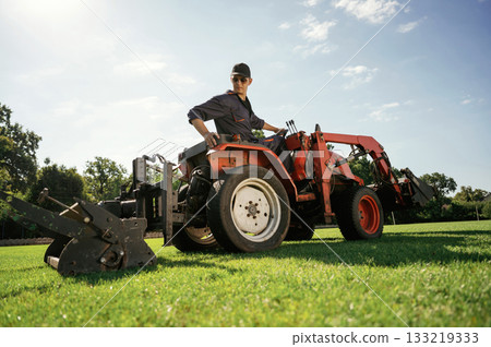 Loan work. Man is with utility tractor with grass cutter and aerator equipment on the field Loan work. Man is with utility tractor with grass cutter and aerator equipment on the field 133219333