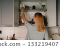 Woman Reaching for Dishes in Kitchen Cabinet 133219407