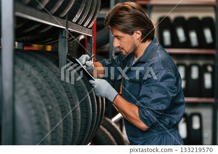 Notepad in hands. Man is in the tire fitting car service 133219570