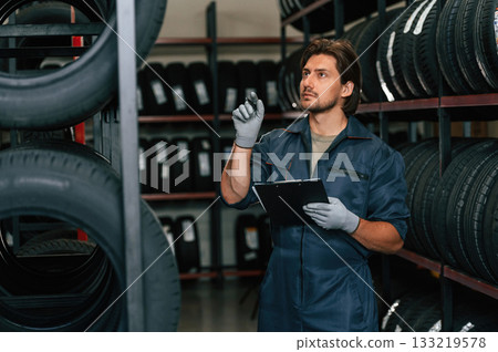 Holding black notepad. Man is in the tire fitting car service Holding black notepad. Man is in the tire fitting car service 133219578