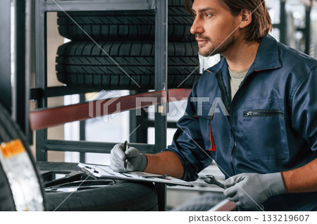 Writing the data into notepad. Man is in the tire fitting car service Writing the data into notepad. Man is in the tire fitting car service 133219607