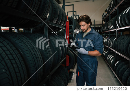 Holding black notepad. Man is in the tire fitting car service 133219620