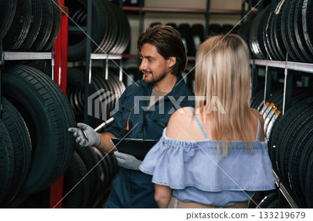 Giving the advice. Woman is in the tire fitting auto shop with worker Giving the advice. Woman is in the tire fitting auto shop with worker 133219679