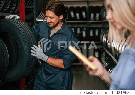 Giving the advice. Woman is in the tire fitting auto shop with worker 133219683