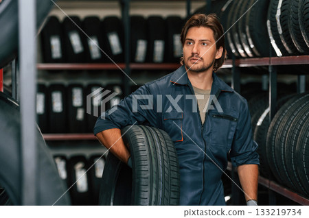Strong worker is with tire. Man is in the tire fitting car service 133219734