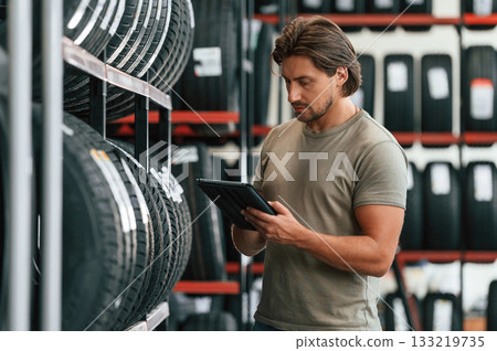Digital tablet in hands. Man is in the tire fitting car service Digital tablet in hands. Man is in the tire fitting car service 133219735
