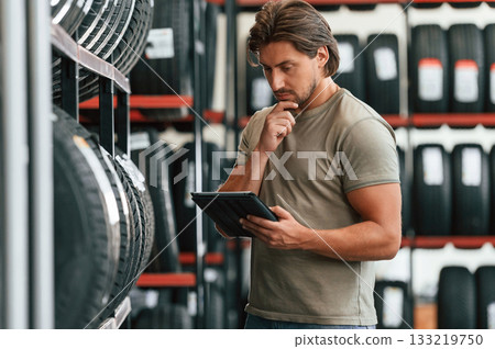 Digital tablet in hands. Man is in the tire fitting car service 133219750