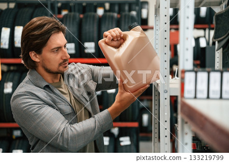 Picking up the oil from the shelve. Man is in the tire fitting car service 133219799